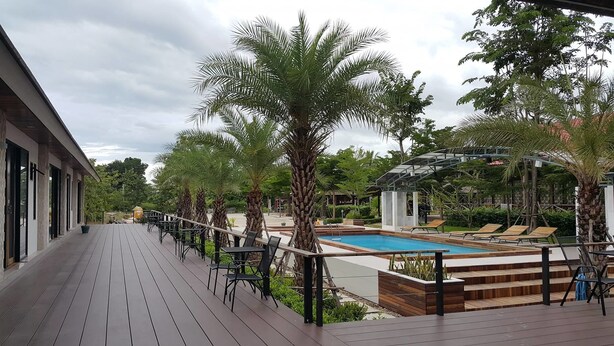 A wooden deck with outdoor seating, a pool, and palm trees. - Ingaun Resort (Lao Khwan)