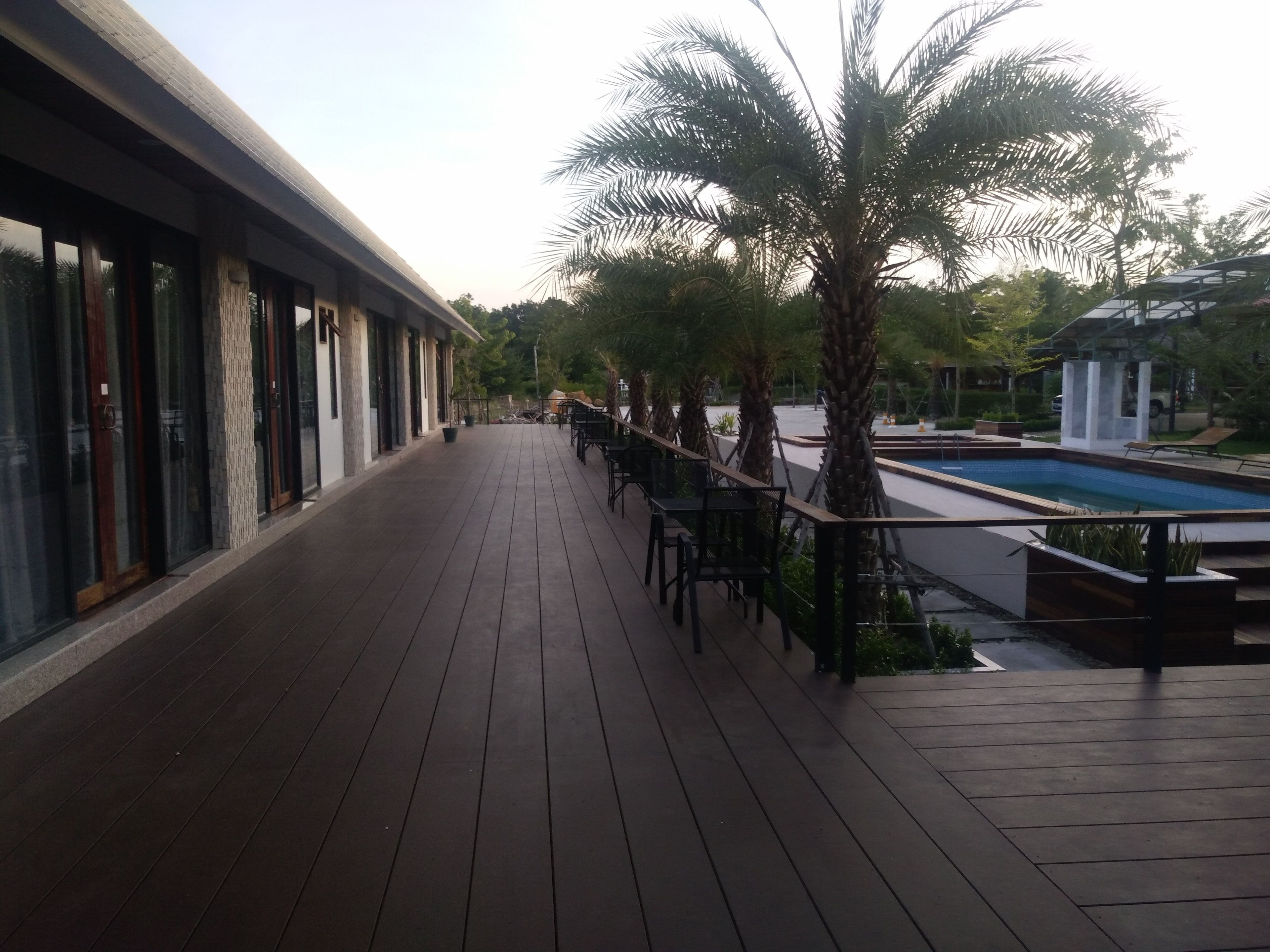 A wooden deck with a pool, palm trees, and a building with large windows.