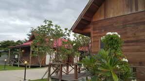 A wooden building with a red roof, surrounded by greenery and a paved walkway. - Ingaun Resort (Lao Khwan)