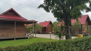 A row of wooden cabins with red roofs, surrounded by greenery and a paved walkway. - Ingaun Resort (Lao Khwan)