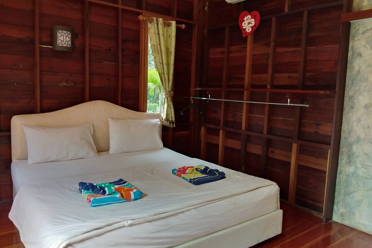 A wooden room with a bed, a window with a curtain, and a wall-mounted air conditioner.