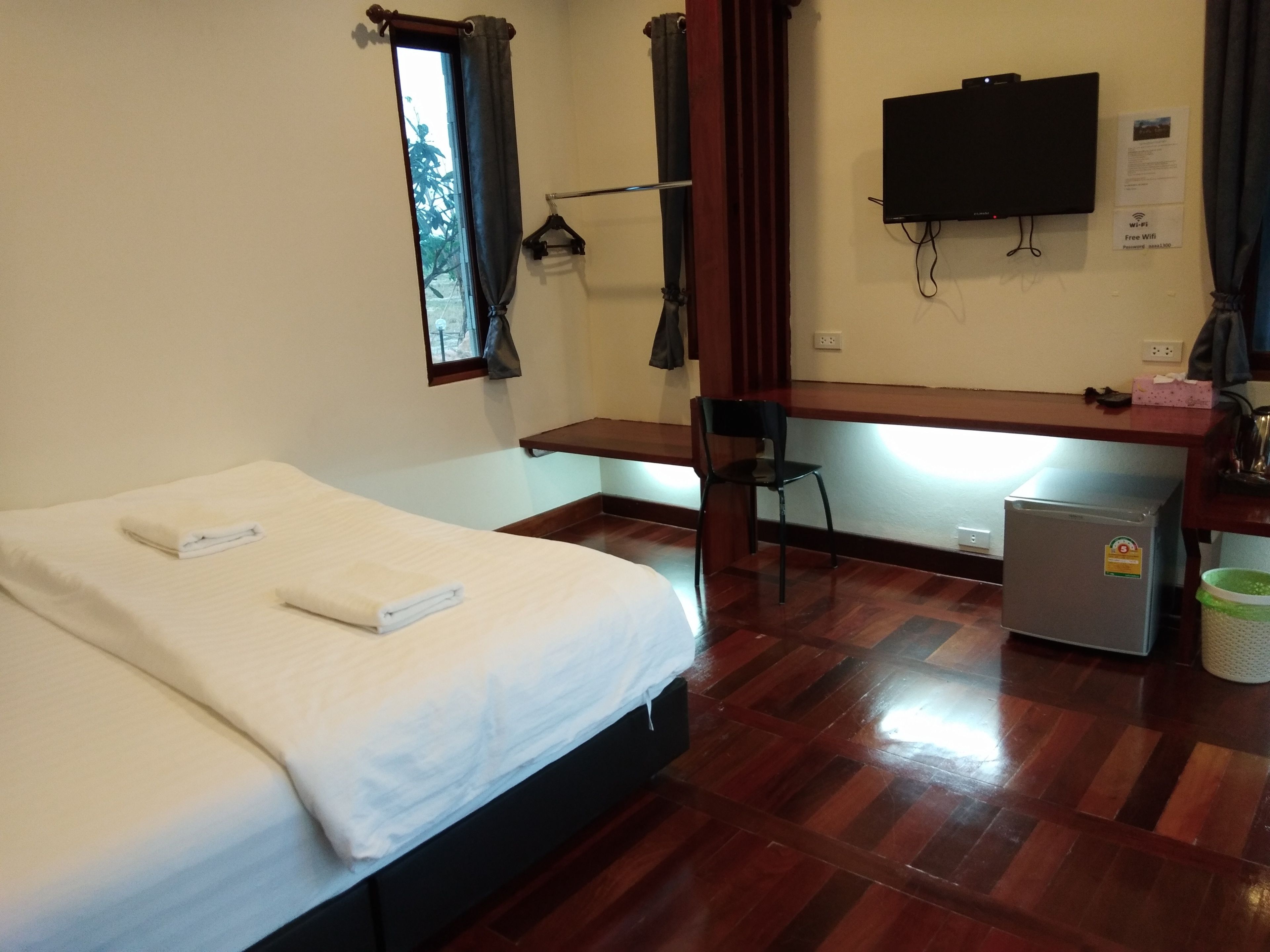 A hotel room with a bed, a desk, a chair, a TV, and a small refrigerator.