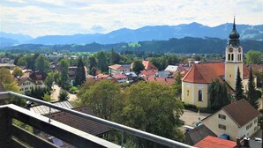 A town with a prominent church tower, surrounded by residential buildings and greenery, with mountains in the background. - Sanosueno 1 - Traumhafter Bergblick (Sonthofen)