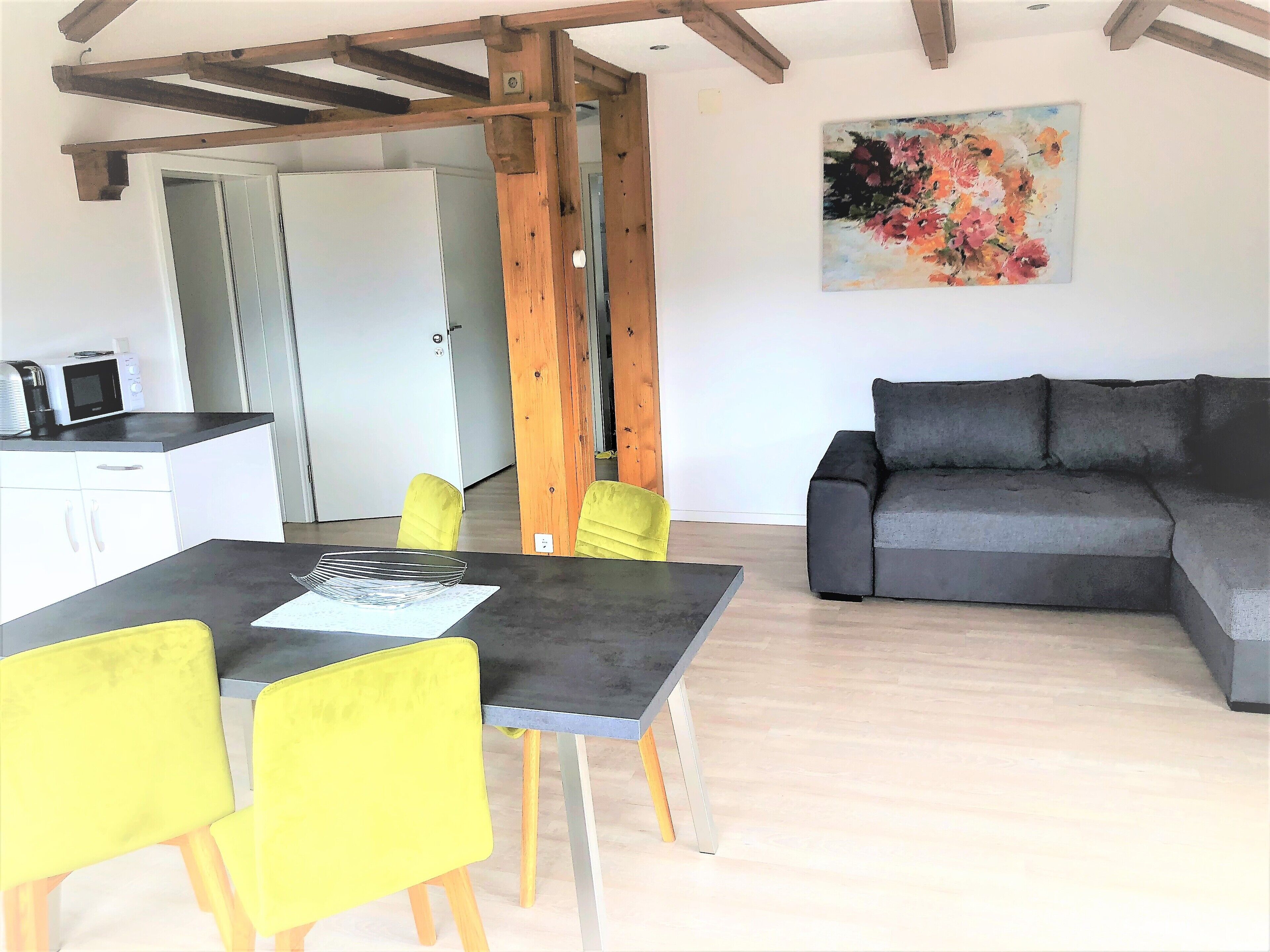 A modern living space with a dining area, a gray sofa, and a wooden ceiling structure.