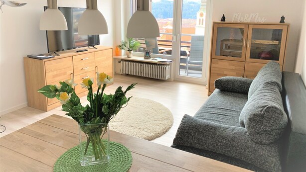 A modern living room with a sofa, a coffee table, and a TV. There is a cabinet with glass doors and a plant on the windowsill. - Sanosueno 2 - Toller Bergblick (Sonthofen)