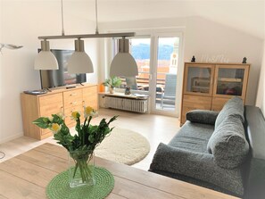 A modern living room with a sofa, a coffee table, and a TV. There is a cabinet with glass doors and a plant on the windowsill. - Sanosueno 2 - Toller Bergblick (Sonthofen)