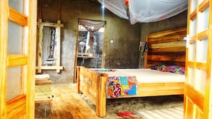Ein rustikaler Holzraum mit einem Bett, einer kleinen Ablage und einem hängenden Moskitonetz.