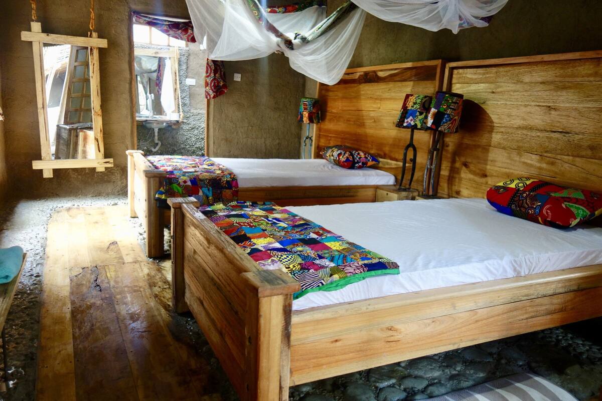 Ein hölzernes Bett mit einer farbenfrohen Stegdecke, eine Holzbank, ein Spiegel und ein Moskitonetz.