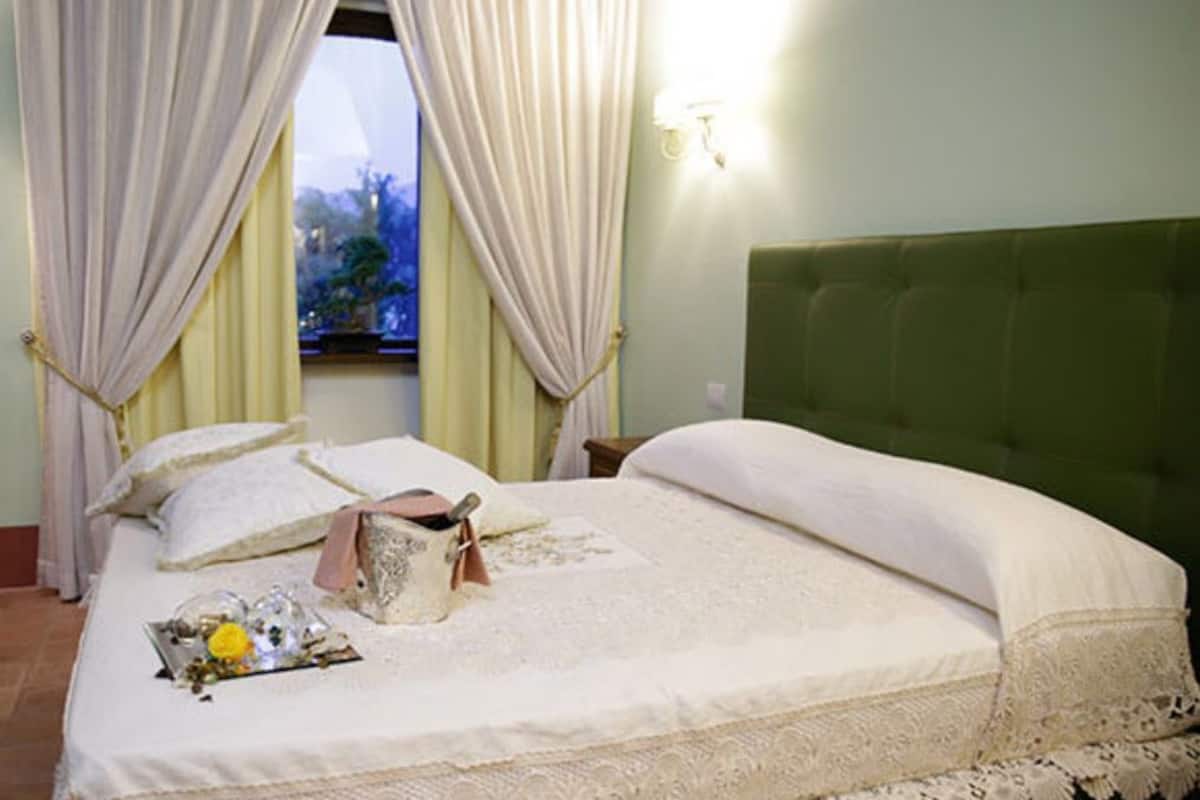 A neatly made bed with a green headboard, a bedside table with a lamp, and a window with curtains.