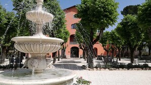 A fountain with water jets in a courtyard with trees and a building in the background. - Villa Floridiana (Anagni)