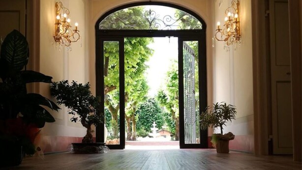 A grand hallway with a wooden floor, a large arched doorway, and potted plants on either side. - Villa Floridiana (Anagni)