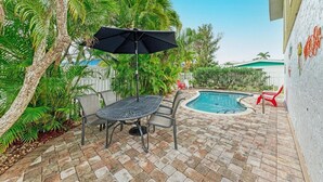 A patio area with a pool, outdoor furniture, and lush greenery. - Dreamscape: North End Pool Home, 2 Blocks to Beach by Anna Maria Life Vacation Rentals (Anna Maria)