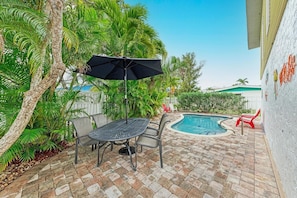 Relax in an outdoor space with a small pool, metal table, and comfortable seating under a large umbrella.