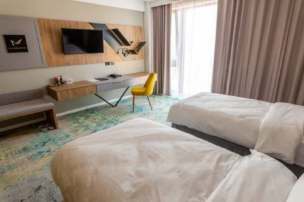 A hotel room with two beds, a desk, a chair, and a TV mounted on the wall.