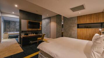 Una habitación de hotel moderna con una cama grande, un escritorio con una silla, un televisor y una estantería empotrada.
