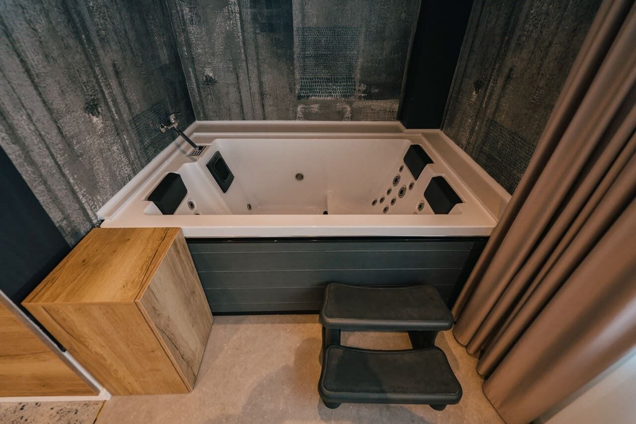 Une salle de bain moderne avec une baignoire rectangulaire, un banc en bois et un tabouret noir.