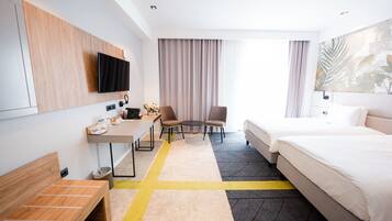 A hotel room with a bed, desk, chairs, a TV, and a large window with curtains.