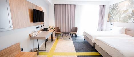 A hotel room with a bed, desk, chairs, a TV, and a large window with curtains.