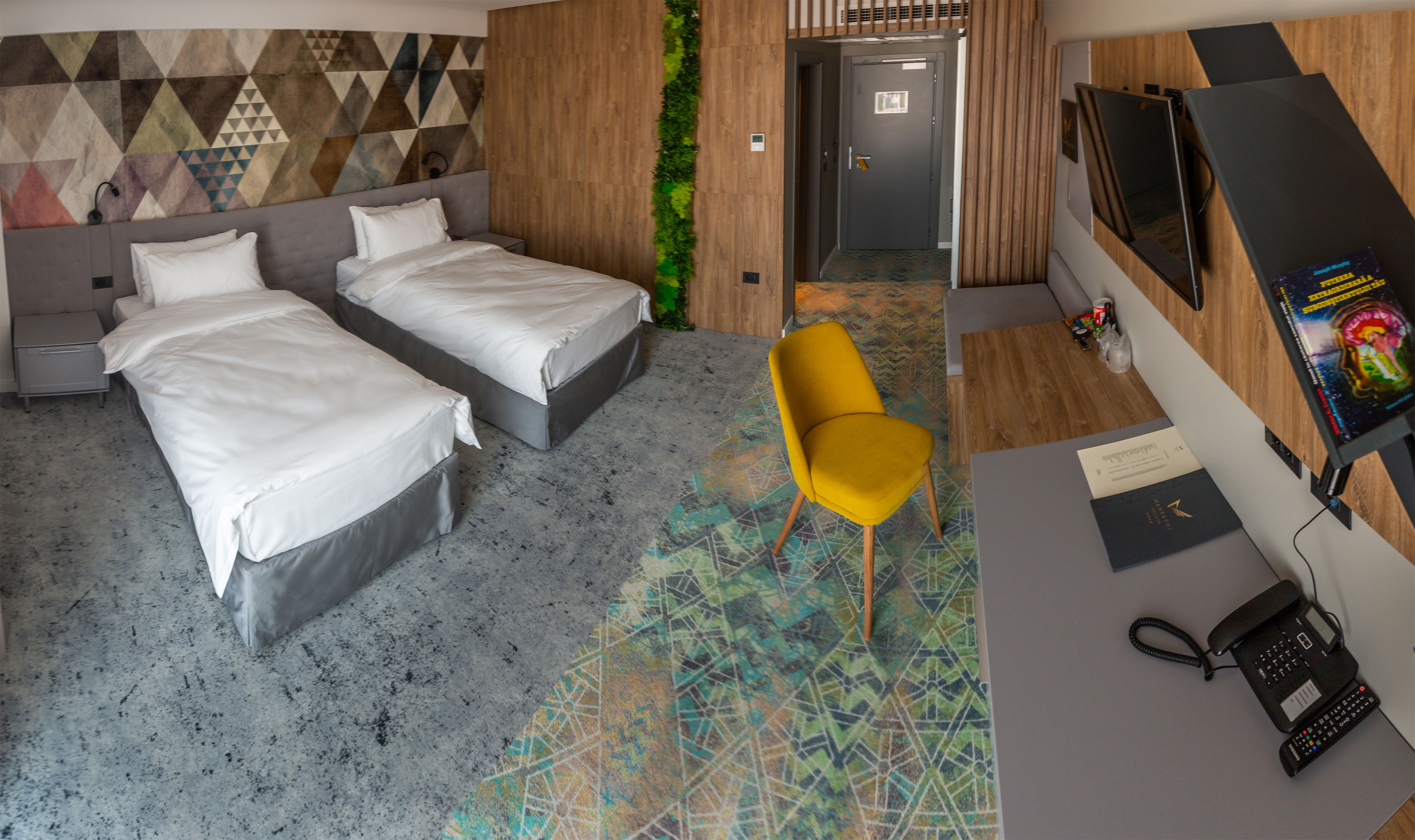 A hotel room with two beds, a desk with a phone, a TV, and a colorful carpet.