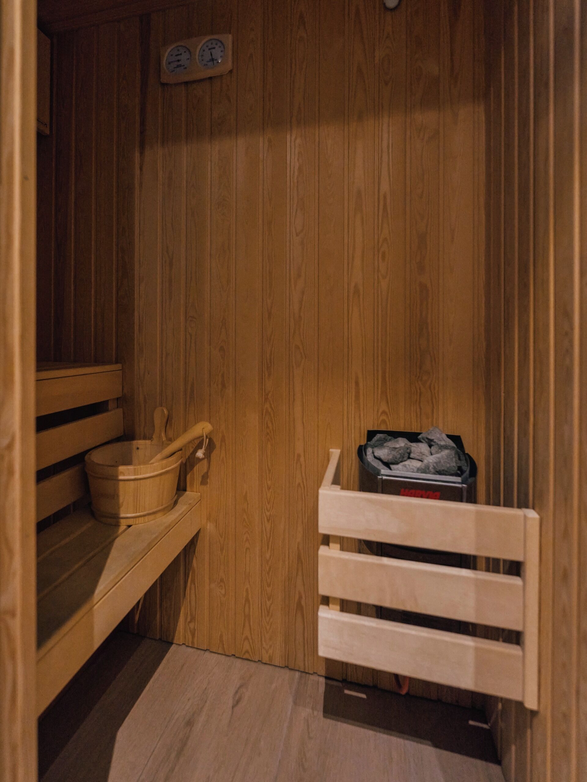A wooden sauna with a wooden bench, a bucket, and a shelf with items.