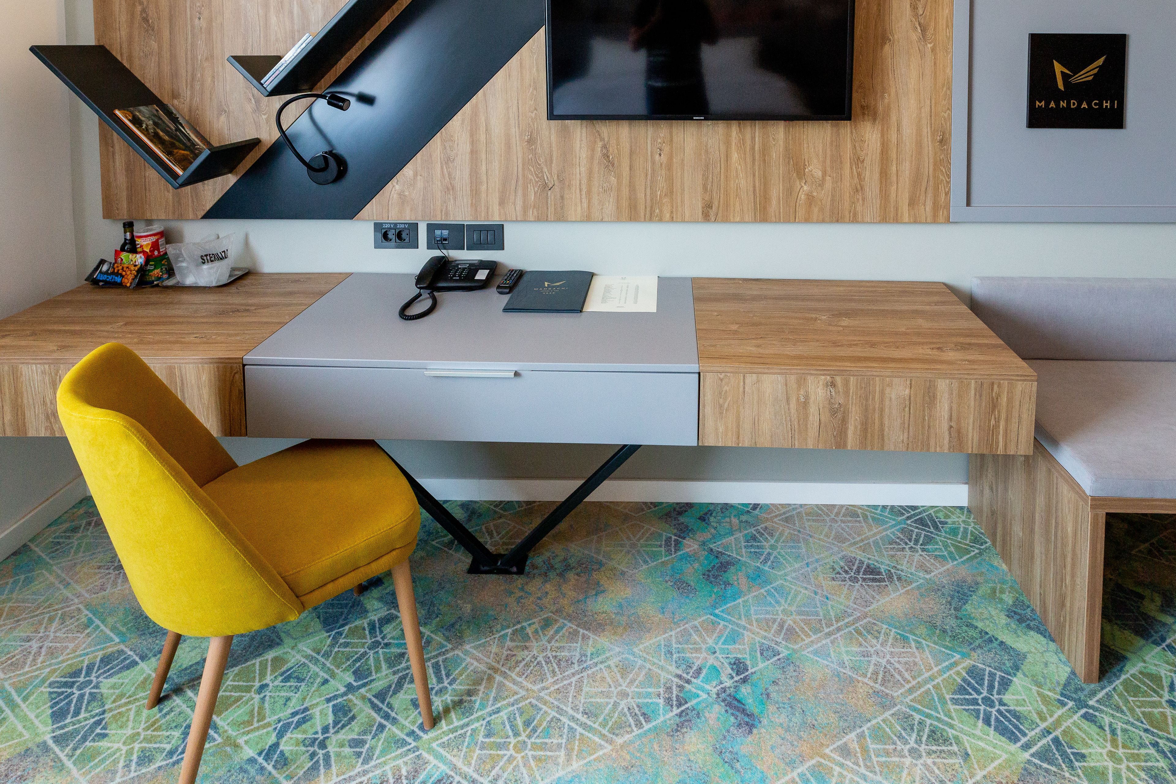 Een modern bureau met een gele stoel, een flatscreen televisie aan de muur en een vloer met een patroon.