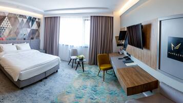 A modern hotel room with a large bed, a desk, a chair, and a television.