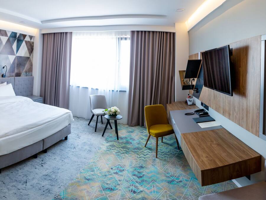 A modern hotel room with a large bed, a desk, a chair, and a television.