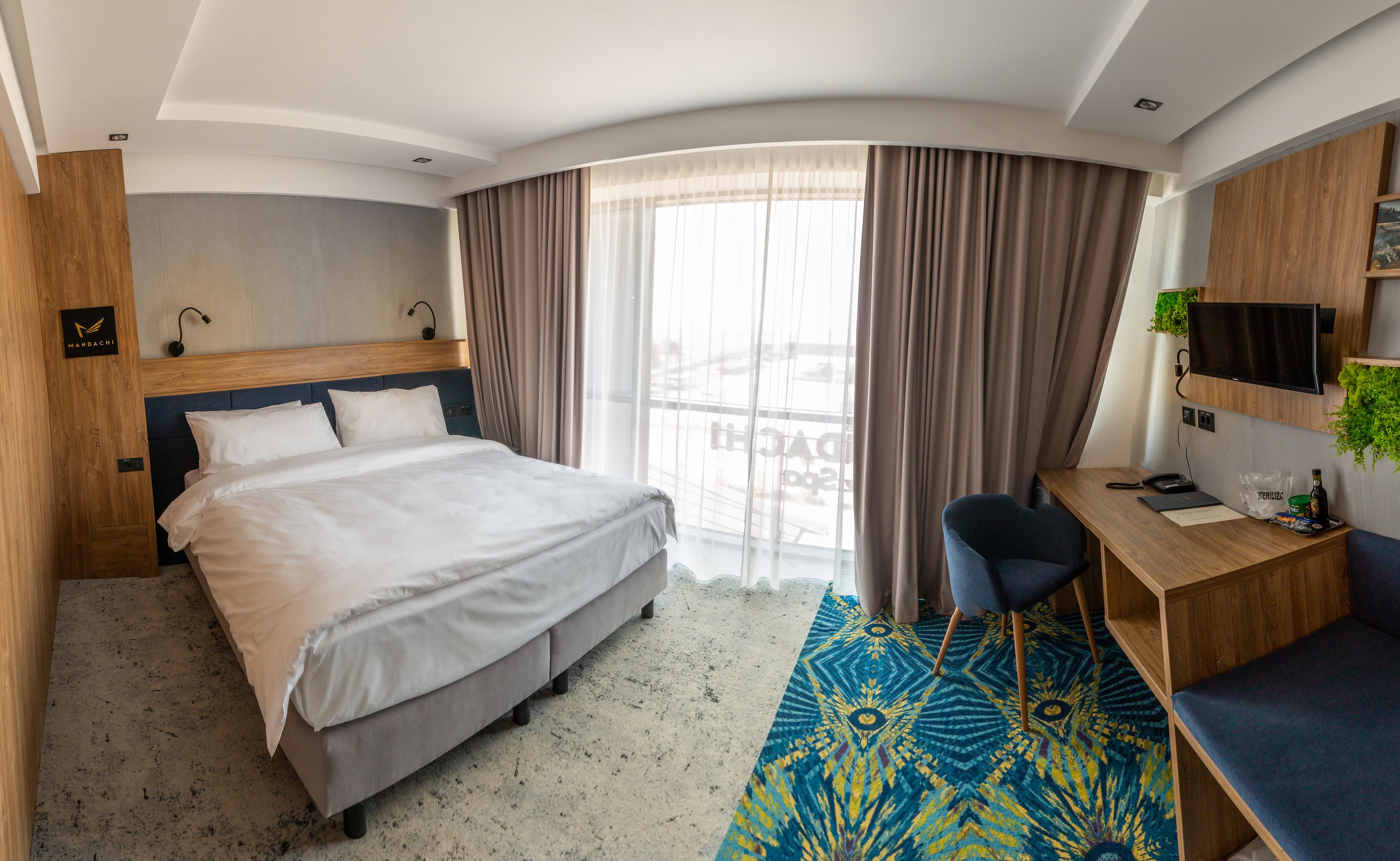 Habitación de hotel con cama, escritorio, silla, televisor y ventana con cortinas.