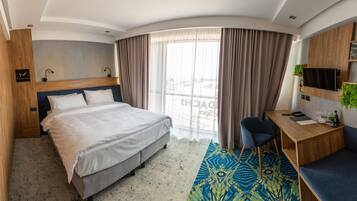 A hotel room with a bed, a desk, a chair, a TV, and a window with curtains.