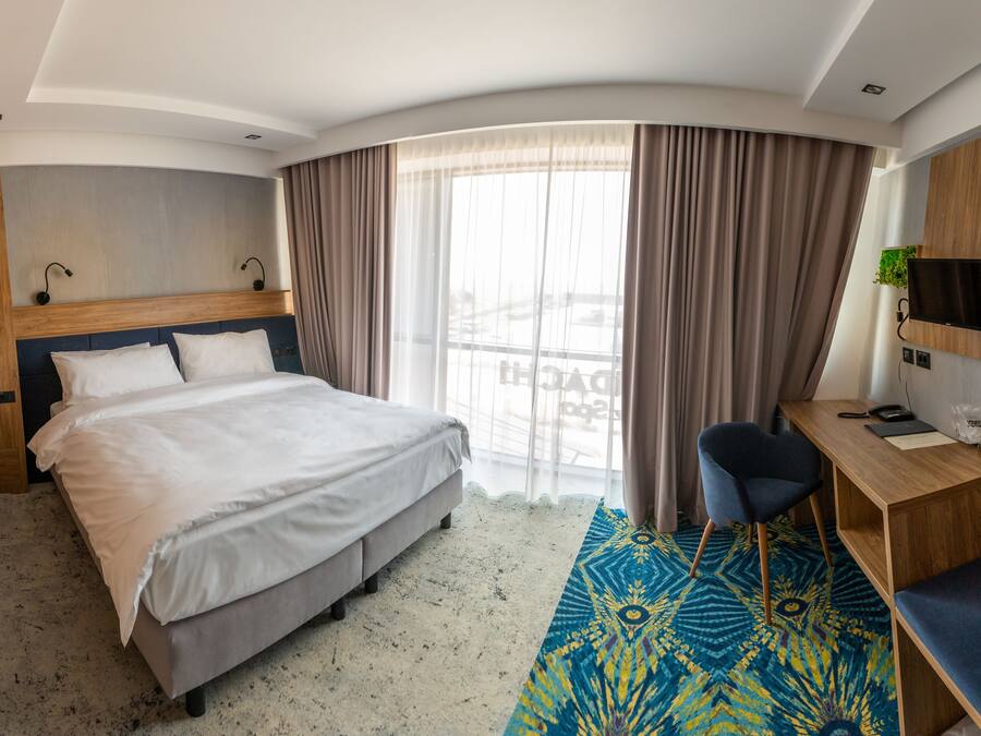 A hotel room with a bed, a desk, a chair, a TV, and a window with curtains.
