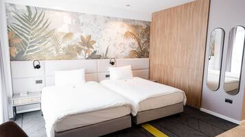 A hotel room with a bed, bedside tables, a mirror, and a wall with a tropical leaf mural.