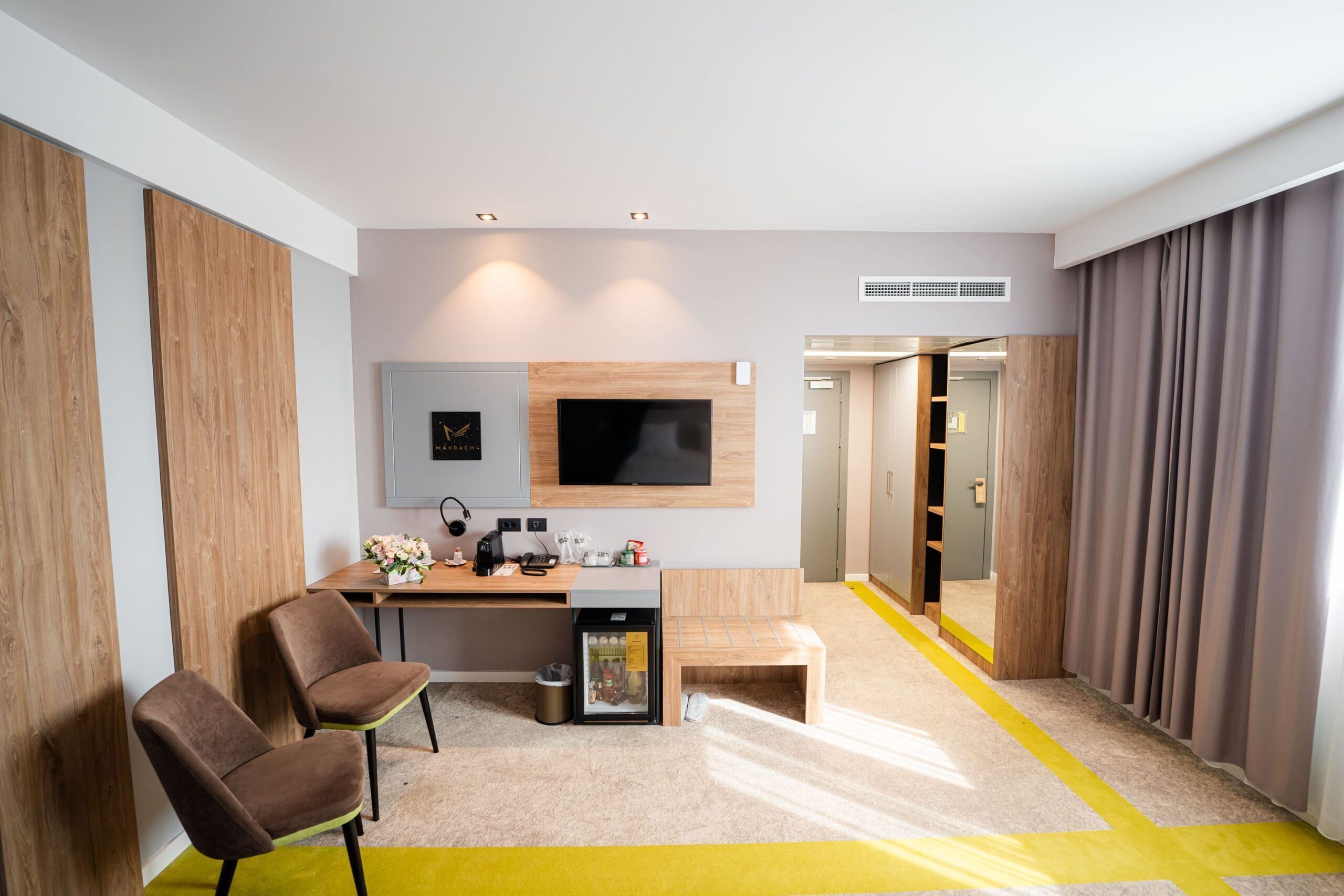 Una habitación de hotel moderna con escritorio, dos sillas, televisor y minibar.