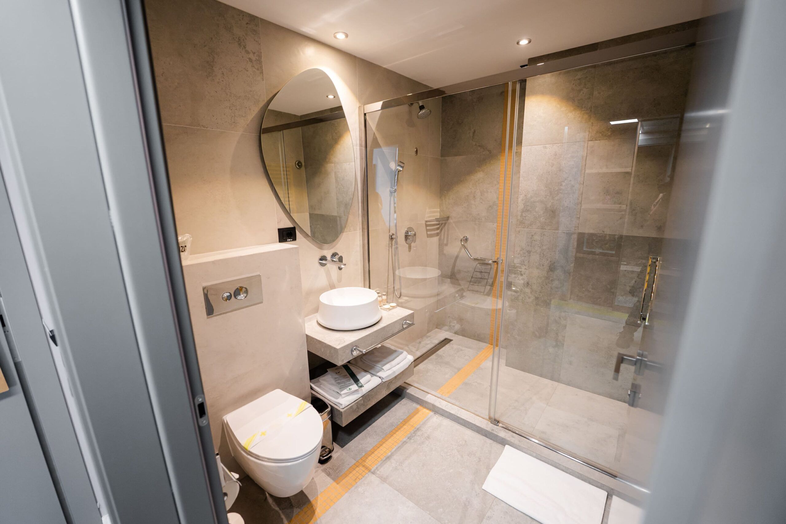 Un baño moderno con ducha de vidrio, espejo redondo y lavamanos blanco.
