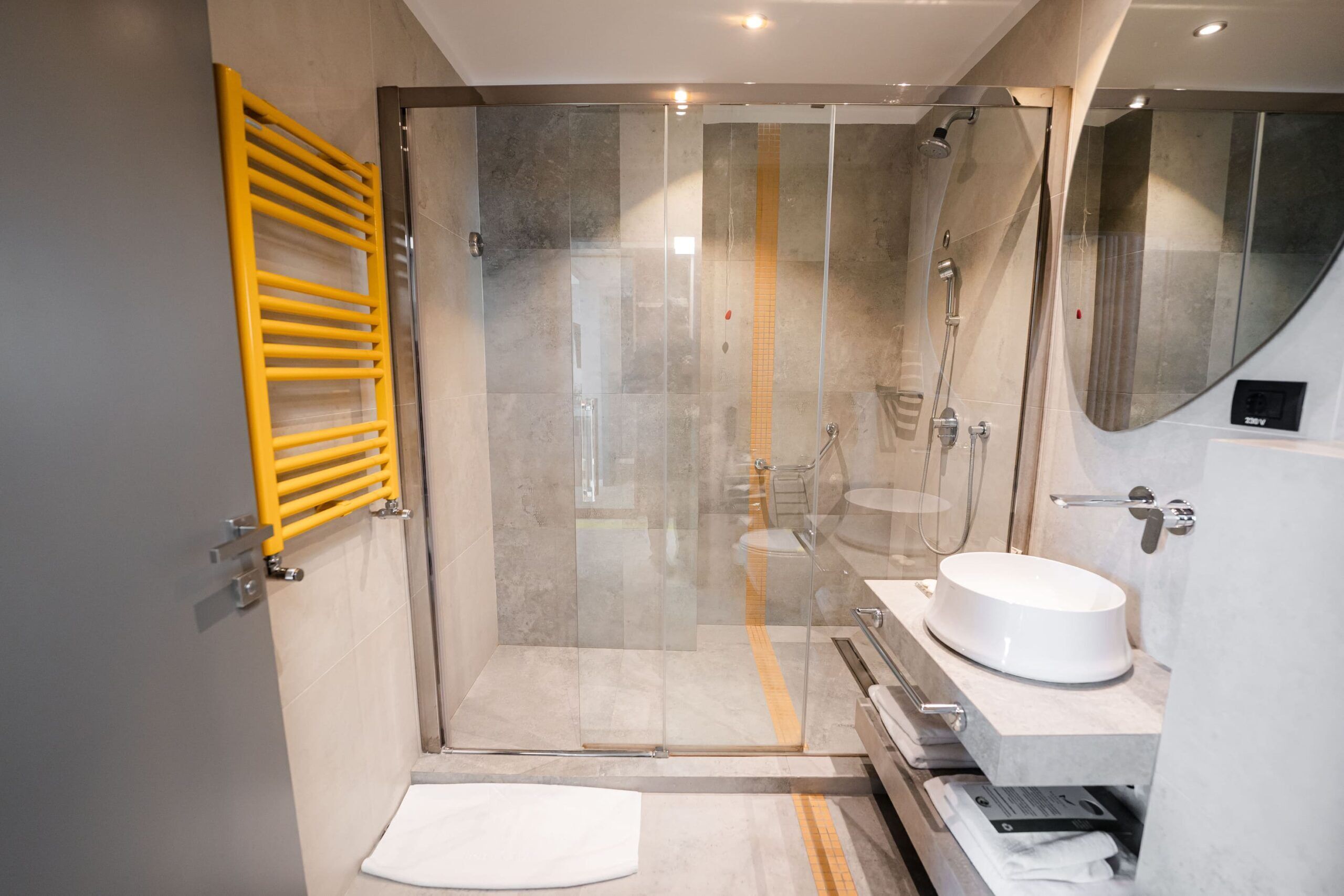 A modern bathroom with a glass shower enclosure, a yellow towel rack, and a white sink.