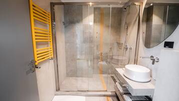 A modern bathroom with a glass shower enclosure, a yellow towel rack, and a white sink.
