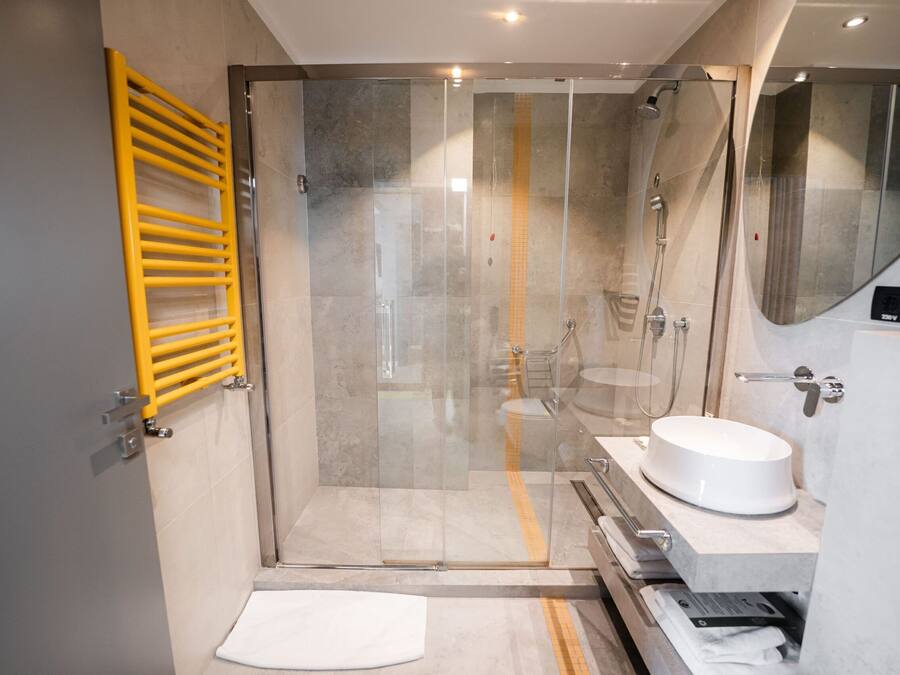 A modern bathroom with a glass shower enclosure, a yellow towel rack, and a white sink.