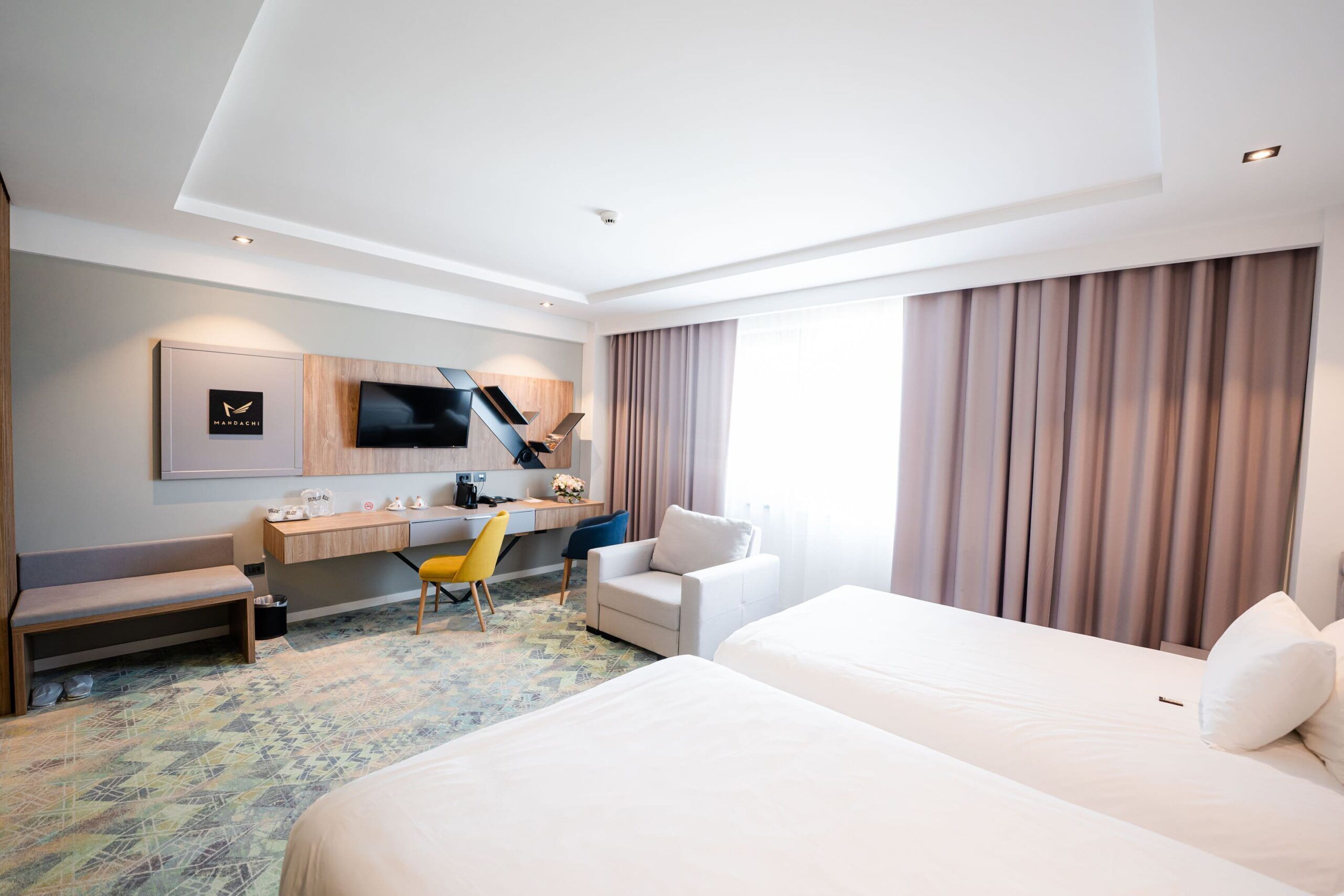 A hotel room with a bed, a desk, a chair, a television, and a window with curtains.