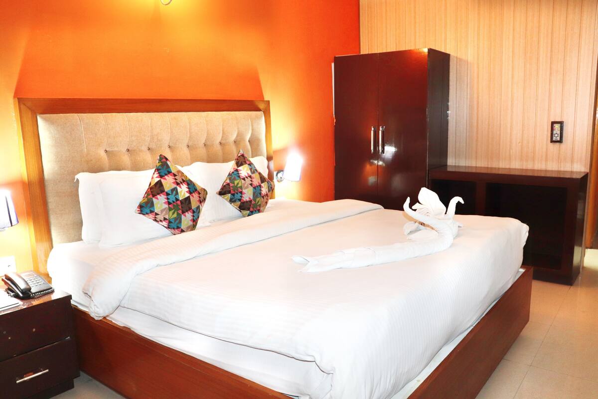 A hotel room with a large bed, a wooden wardrobe, and a bedside table with a phone.