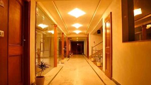 Un pasillo de hotel con una puerta de madera a la izquierda, paredes de vidrio y una planta en maceta.