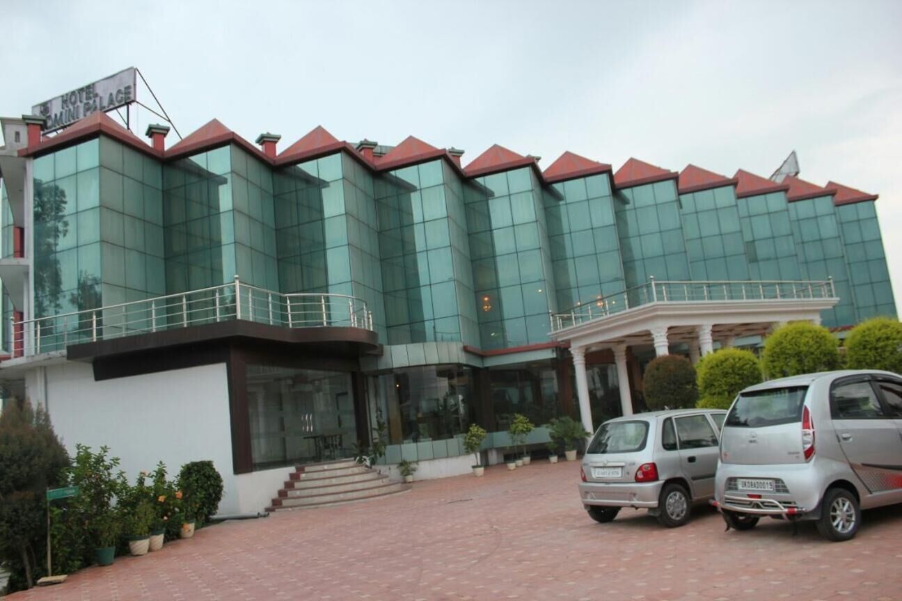 A modern hotel with a glass facade and a red roof. There are two cars parked in front.
