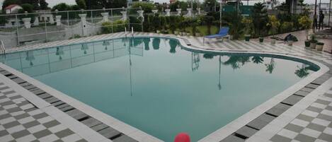 Una piscina con suelo a cuadros, rodeada por una cerca y follaje.