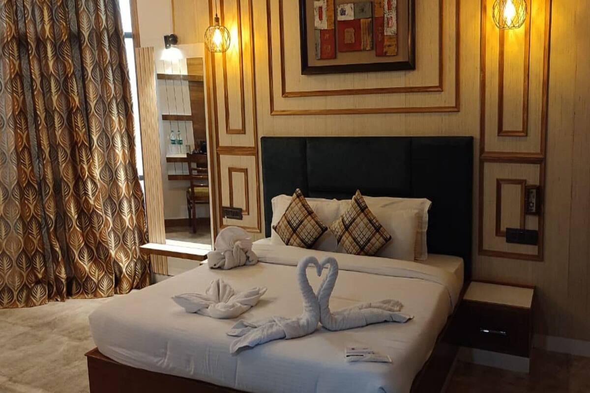 A hotel room with a neatly made bed, a headboard, a bedside table, and a wall-mounted light fixture.