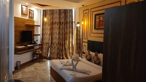 Habitación de hotel con cama, escritorio, televisor y cortina con estampado de hojas.