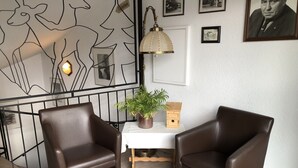A room with two brown leather chairs, a small table with a potted plant, a wooden birdhouse, and a wall with framed pictures and a light fixture. - Hotel-Restaurant Reher Hof (Hagen)