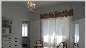 A bedroom with a bed, dresser, two chairs, a glass table, and a chandelier. - Cascina Luvot (Melazzo)