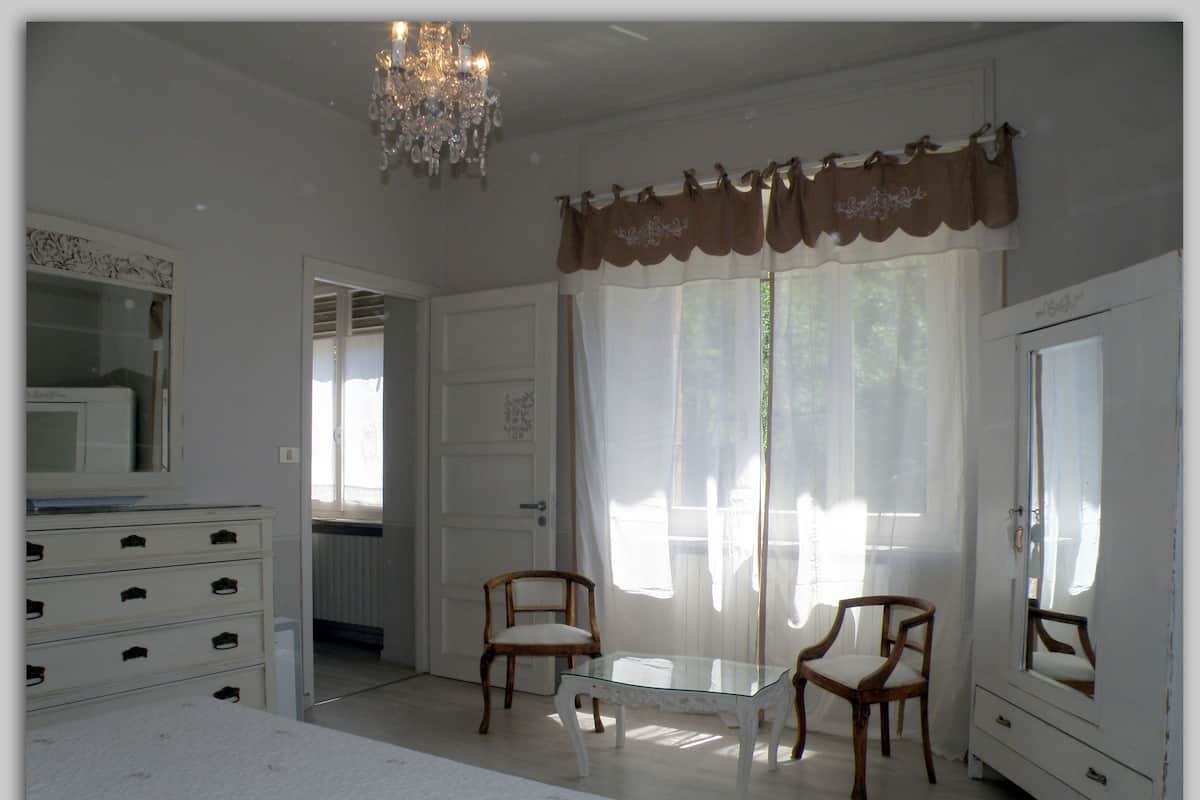 A bedroom with a bed, dresser, two chairs, a glass table, and a chandelier.