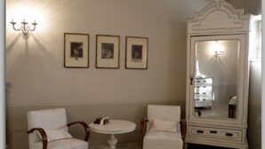 A room with two white armchairs, a small round table, and a large white mirror cabinet with a light source inside. - Cascina Luvot (Melazzo)