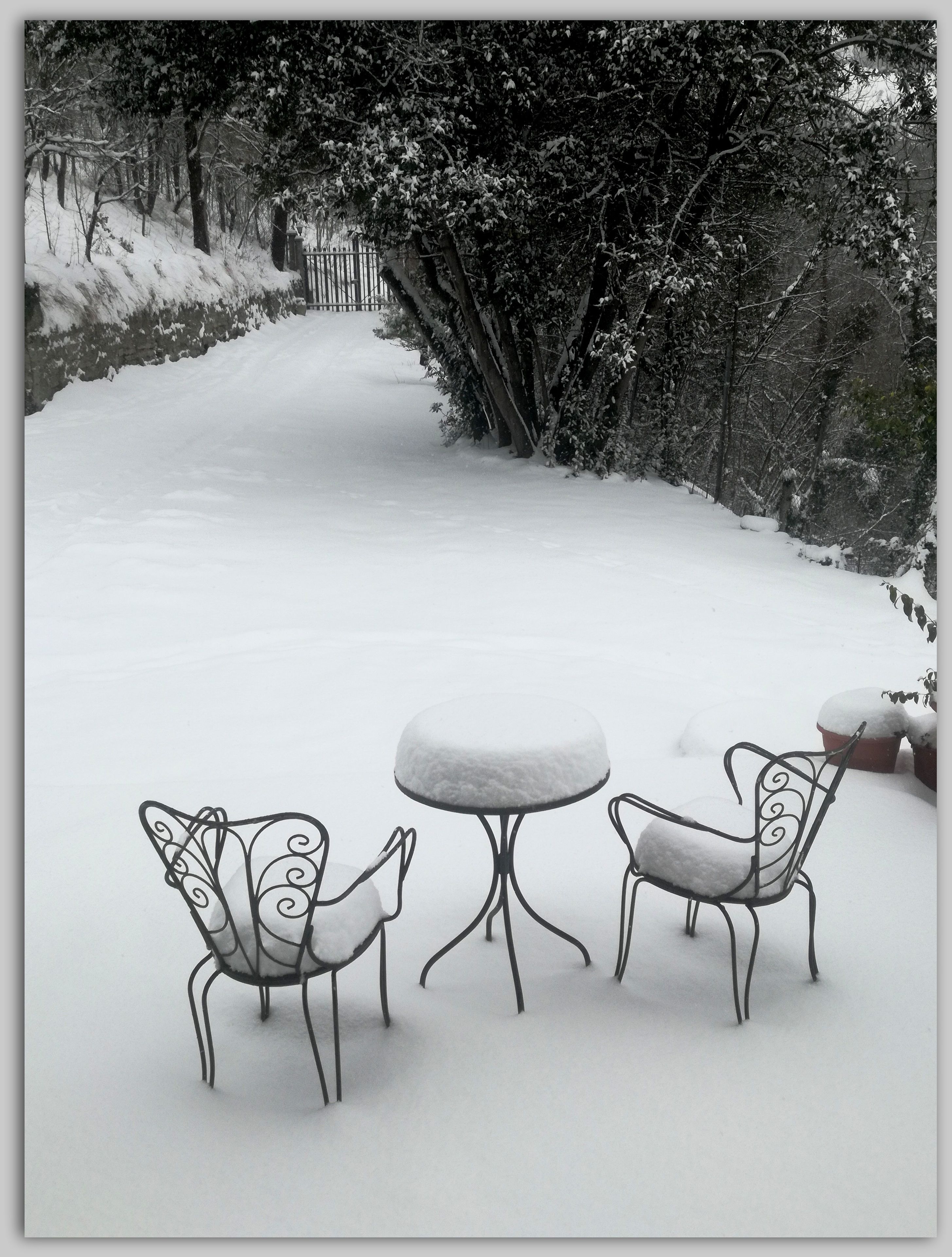 Un espacio al aire libre cubierto de nieve con sillas y una mesa de metal.