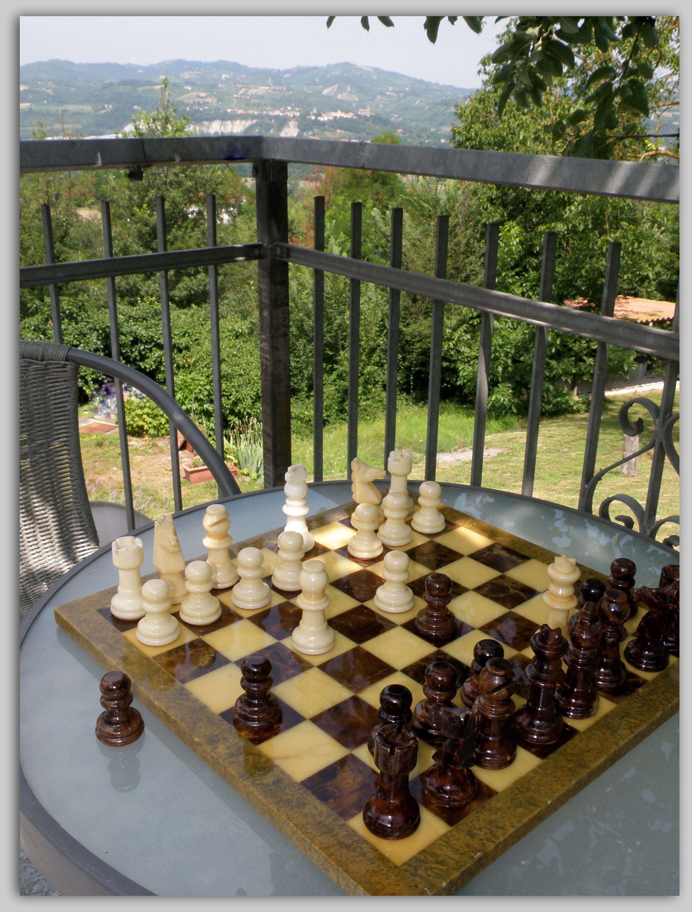 A chessboard on a glass table with a scenic view of hills and greenery in the background.