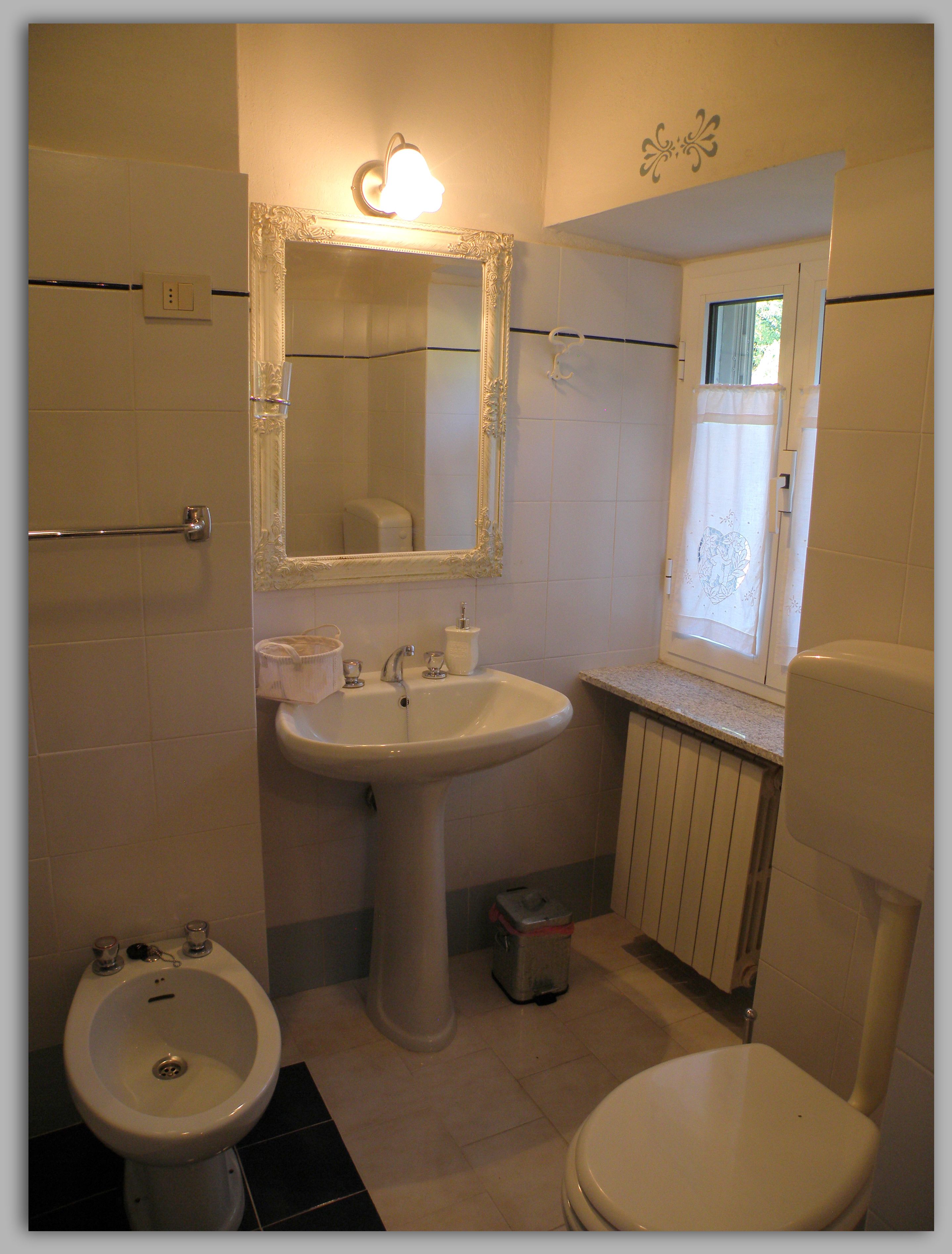 Un baño con lavamanos pedestal, inodoro, bidé y espejo con luz.